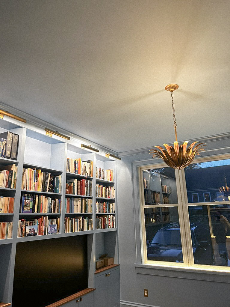Blue color-drenched den with built-in bookshelves, brass Visual Comfort picture lights, and a sculptural gold leaf chandelier — new build interior design Connecticut